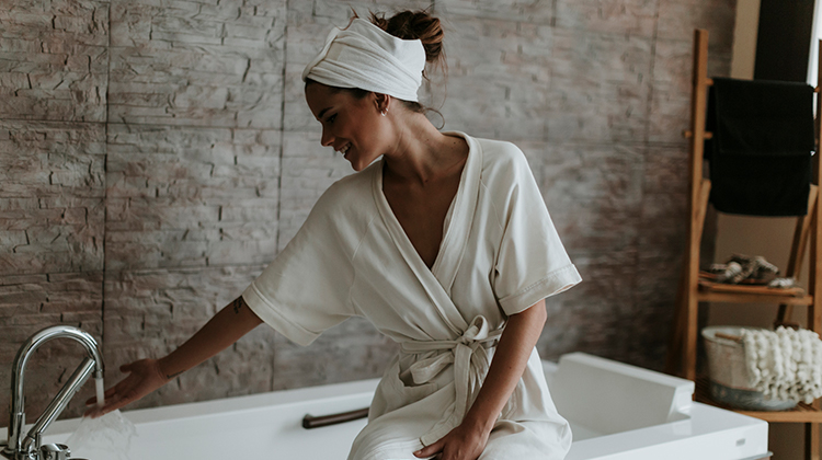 Woman in a robe turning on her bathtub Woman in a robe turning on her bathtub
